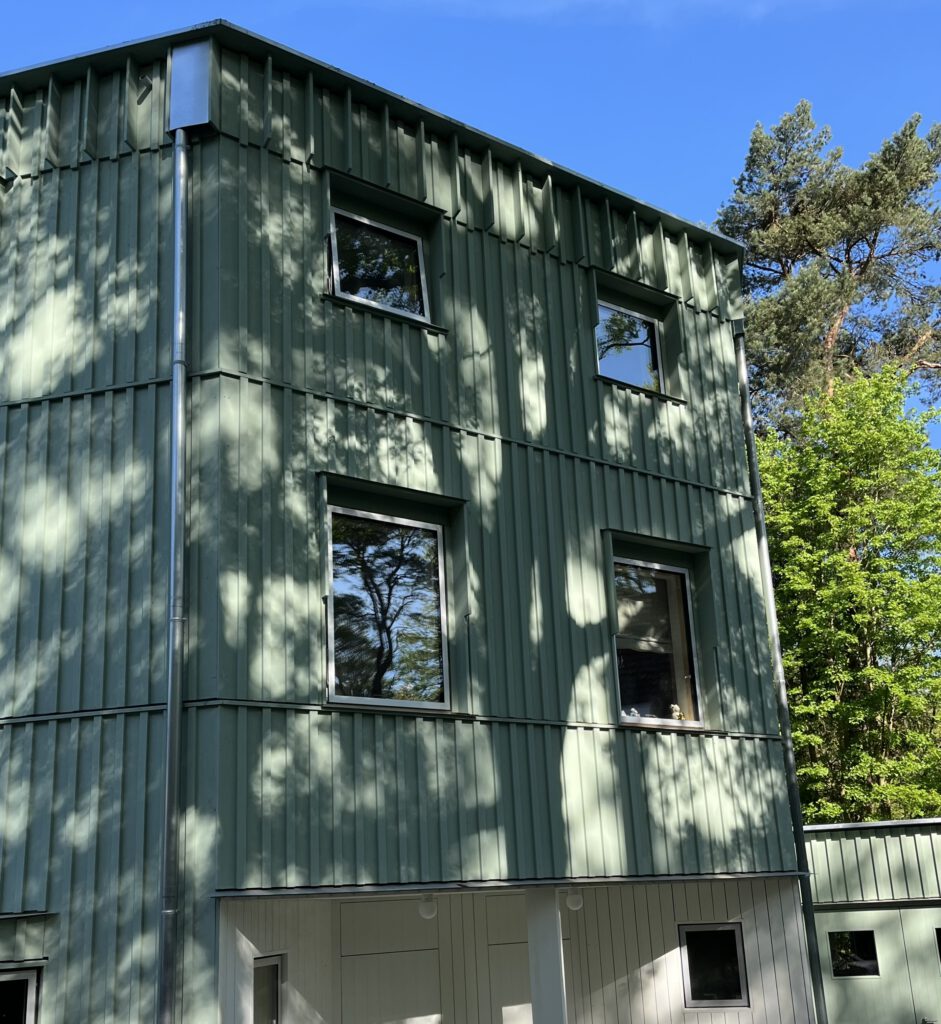 Holzfassade eines zweigeschossigen Holzbaus zwischen Bäumen